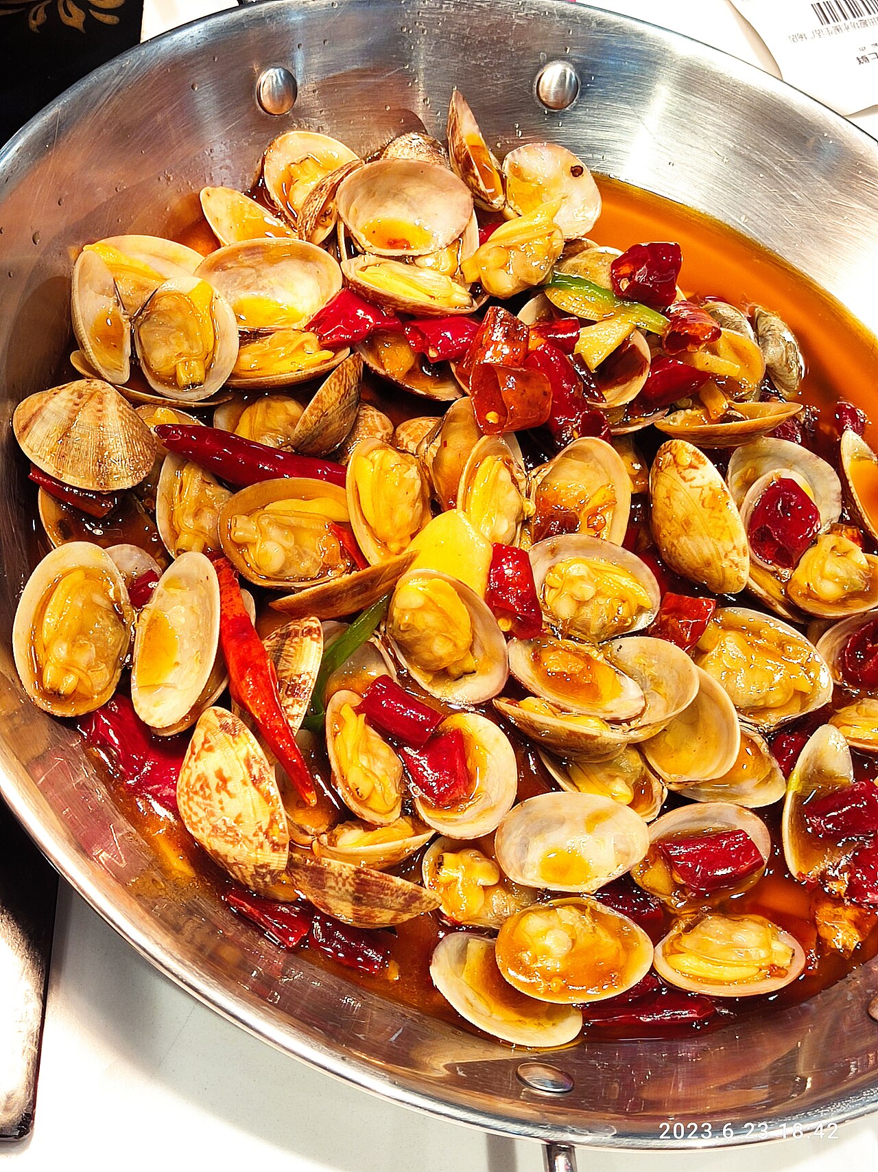 Cooked clams in open shells with dried red chillies and scallions in a metal serving pan