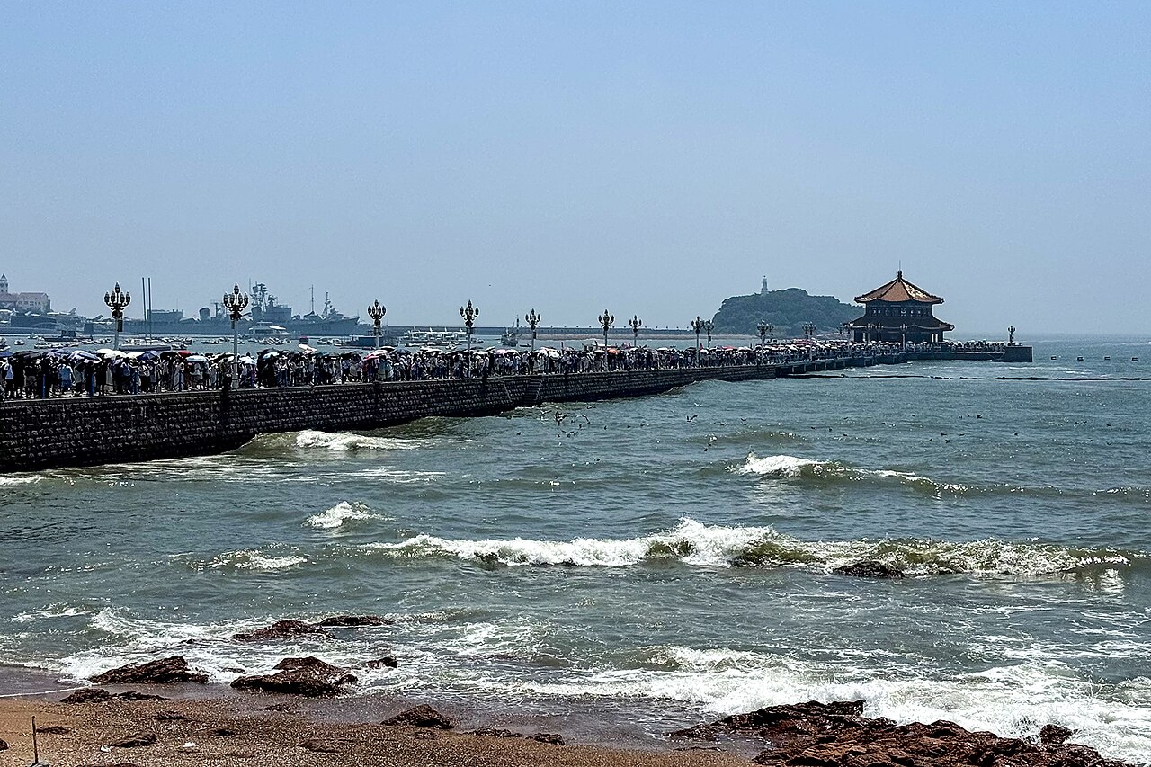 Visitors walking along Zhanqiao Pier toward its pavilion beside Qingdao Bay